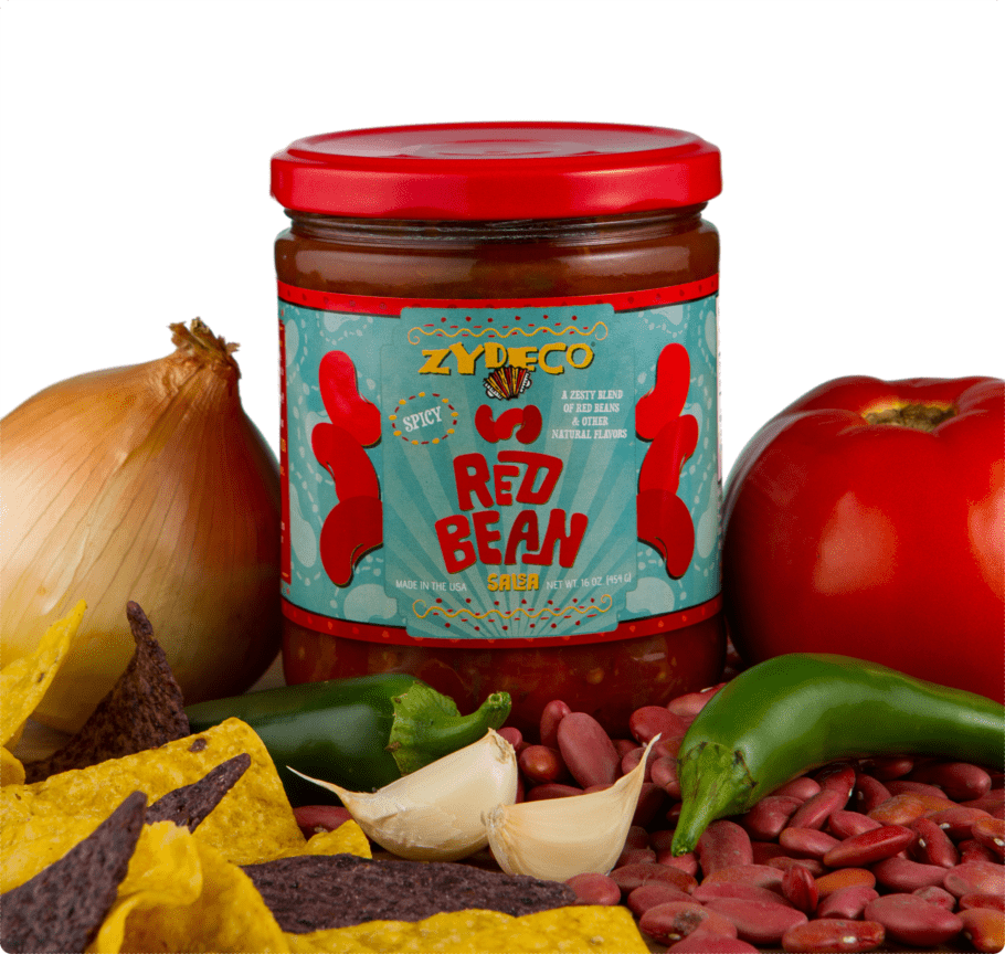 Studio product photograph of a jar of Zydeco Spicy Red Bean Salsa featuring its signature accordion logo surrounded by a large yellow onion, a glossy red tomato, and fresh green jalapeños on a bed of red beans and colorful tortilla chips