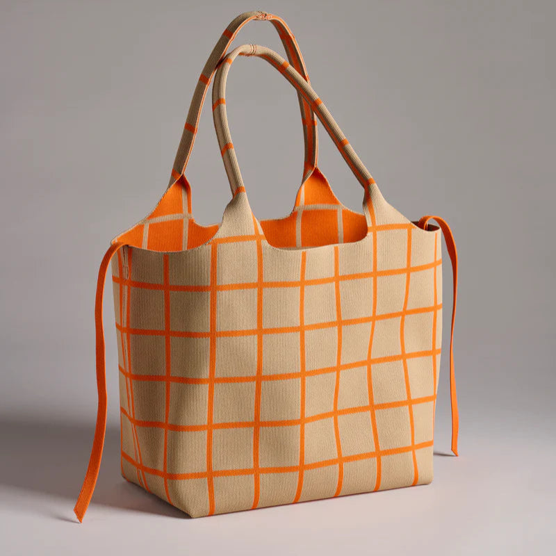 Knitted textile tote bag featuring a beige base with a vibrant orange grid pattern, matching thin side ties, and dual integrated handles positioned in a minimalist studio setting