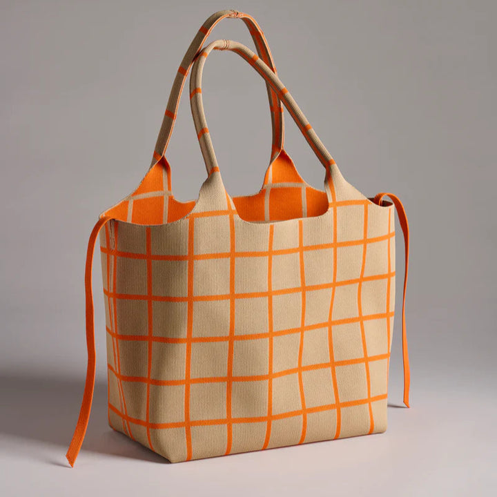 Knitted textile tote bag featuring a beige base with a vibrant orange grid pattern, matching thin side ties, and dual integrated handles positioned in a minimalist studio setting