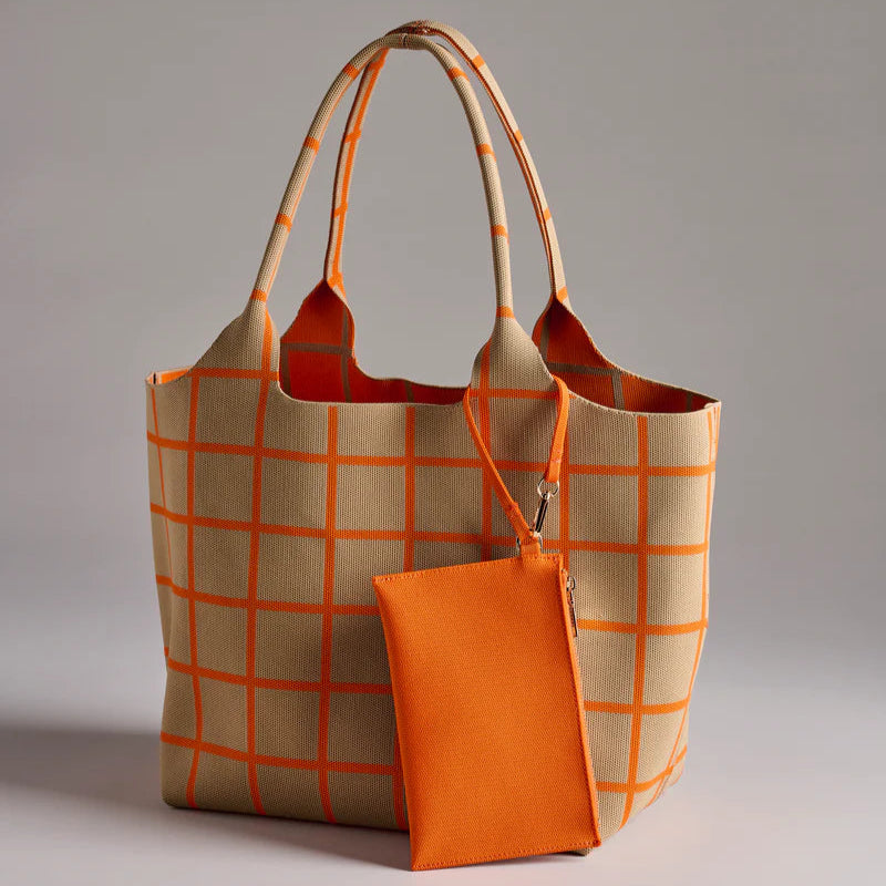 Knitted fabric tote bag and matching detachable zip pouch featuring a vibrant orange windowpane grid pattern on a beige textured base set against a neutral grey studio background