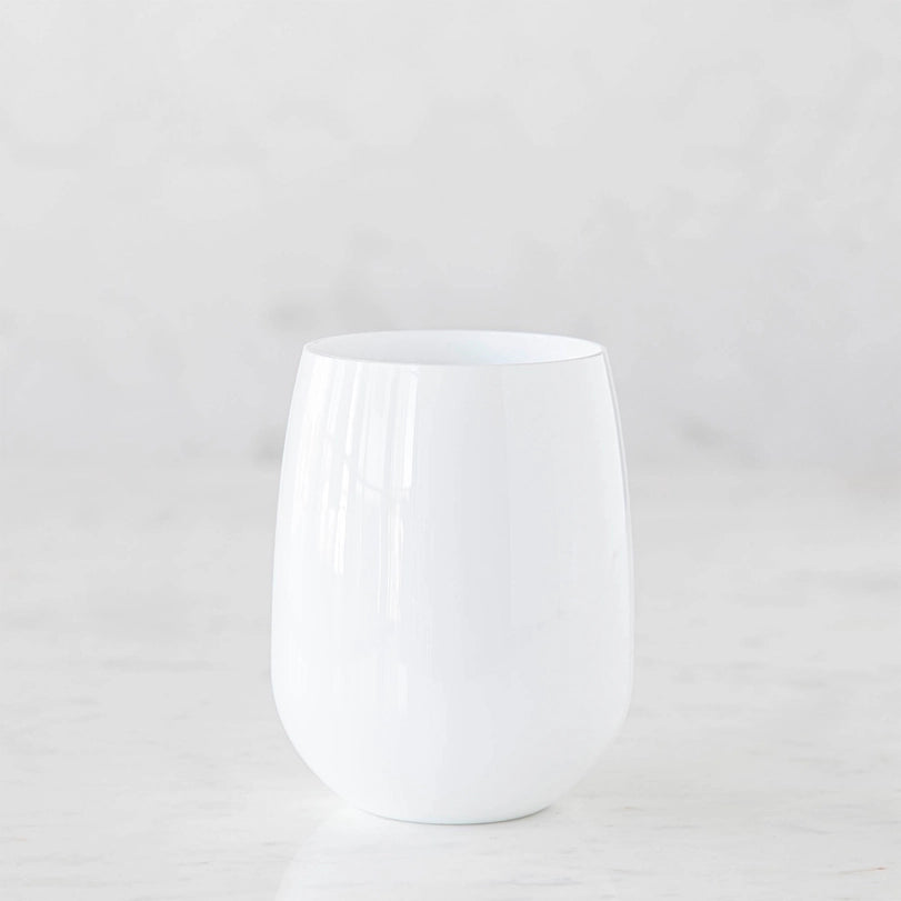 Studio photograph of a stemless opaque white glass tumbler on a white marble surface featuring a smooth curved silhouette and subtle vertical light reflections against a minimalist background