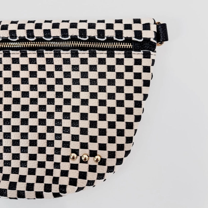 Photograph of a black and white checkered patterned bag on a white background featuring a metallic gold zipper and three small round gold studs on the pebbled texture
