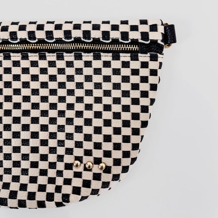 Photograph of a black and white checkered patterned bag on a white background featuring a metallic gold zipper and three small round gold studs on the pebbled texture