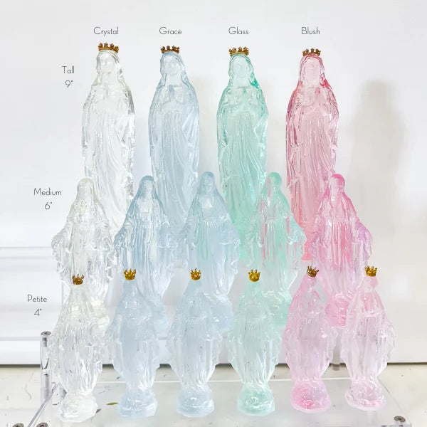 Translucent glass Virgin Mary figurines arranged on a tiered display stand in pastel blush pink and mint green hues featuring tiny gold crowns and varying heights from four to nine inches