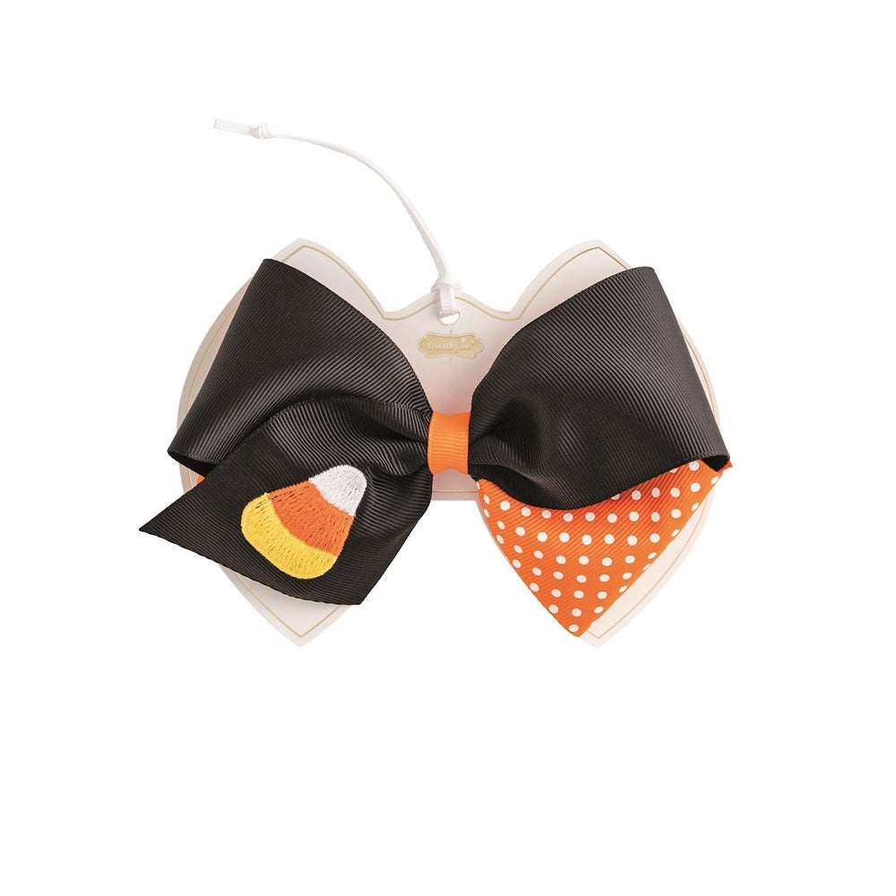 Grosgrain ribbon hair bow by Mud Pie features a large black Halloween hair accessory with an embroidered candy corn, orange polka dot accents, and a bright orange center knot on a white display card