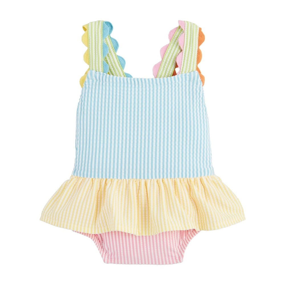 Product photograph of a multi-colored seersucker baby swimsuit on a white background featuring blue and yellow pastel stripes, a pink bottom, and vibrant scalloped rickrack trim along the shoulder straps