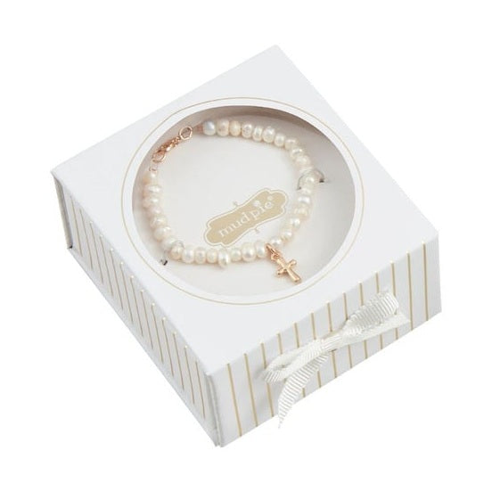 Product photograph by Mud Pie featuring a white freshwater pearl bracelet with a gold-tone cross charm displayed inside a gold-striped white gift box accented with a white grosgrain ribbon bow