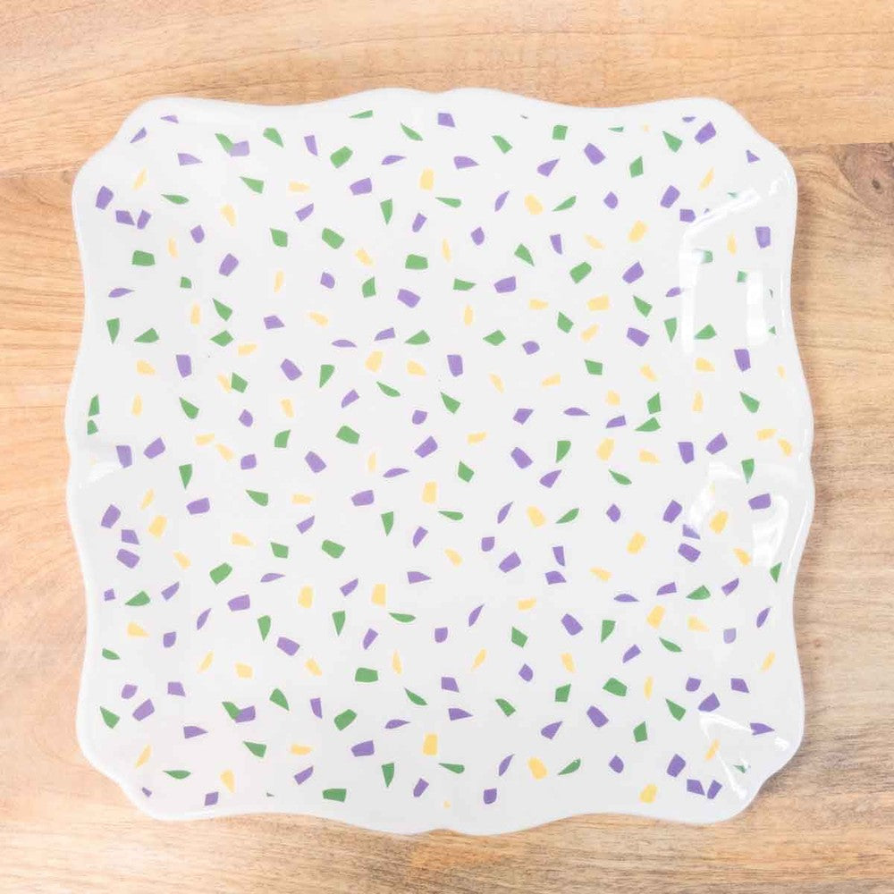 Ceramic square serving platter on a light wood surface featuring a vibrant confetti pattern of purple, green, and yellow geometric flecks across a glossy white base with a decorative scalloped rim