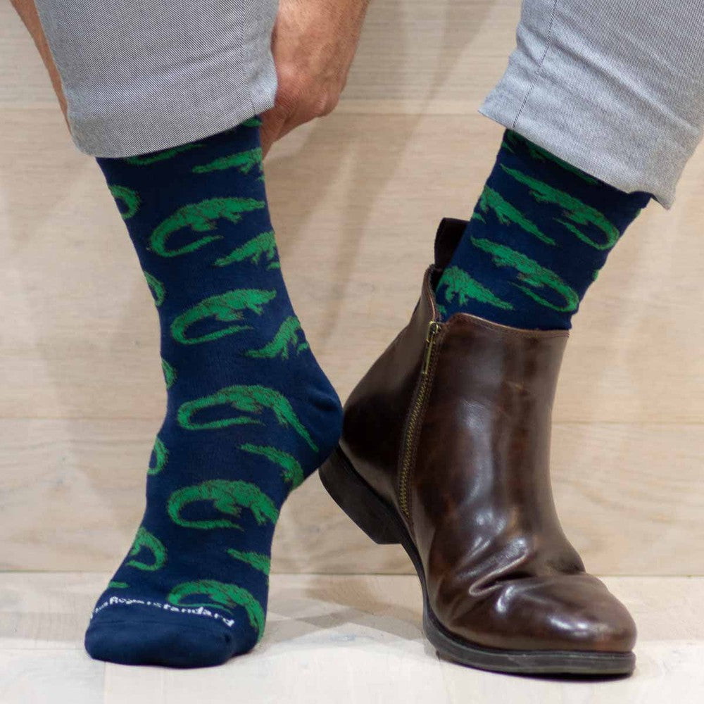 Textile socks featuring the pattern of Vincent van Gogh's Wheatfield with Crows with vibrant green impressionist strokes and a navy blue base worn with a polished brown leather zip-up boot on a light wood background