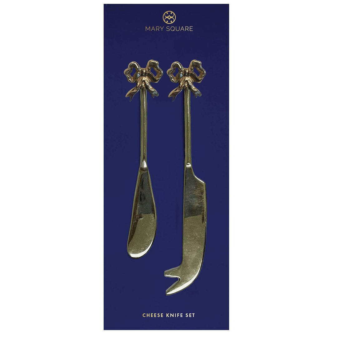 Gold-toned stainless steel cheese knife set by Mary Square featuring two serving utensils with ornate bow-shaped handles and reflective blades on a navy blue product card