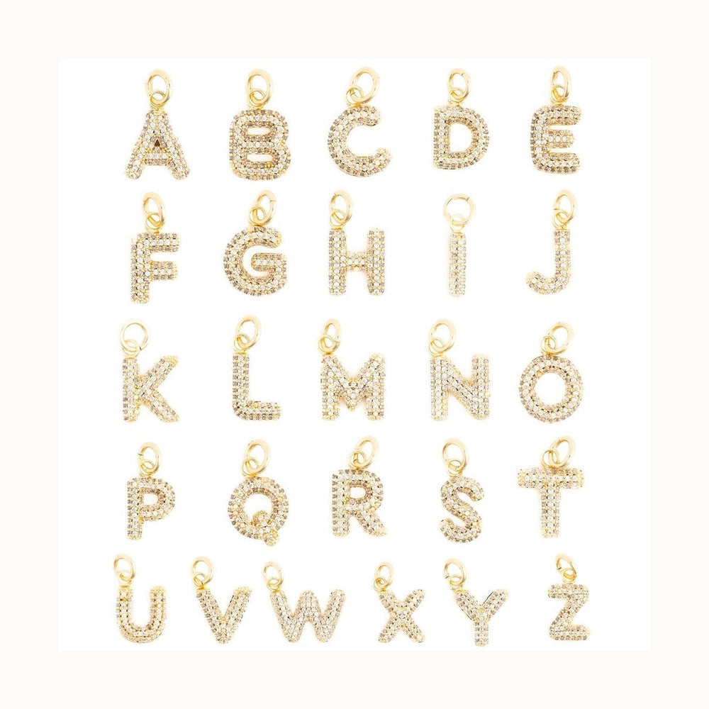Gold-plated jewelry charms encrusted with pavé-set cubic zirconia stones featuring a complete alphabet and special accented characters arranged in rows on a white background with individual gold jump rings