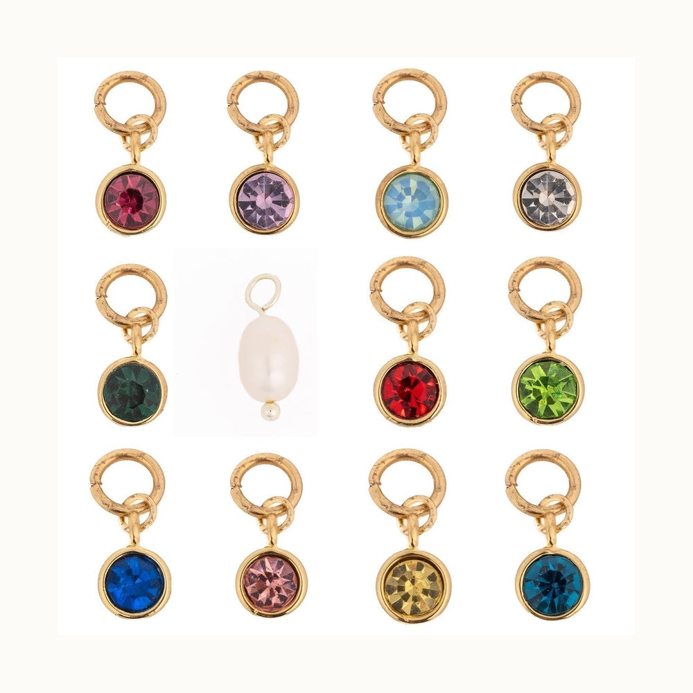 Studio photograph of twelve assorted jewelry charms featuring vibrant faceted round crystals and a single white drop pearl suspended from textured gold and silver rings in a grid layout on a white background