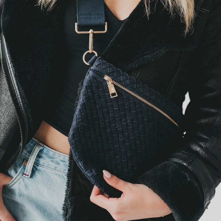 Digital photograph of a woman wearing a black woven crossbody bag featuring gold-toned hardware, a black shearling-lined jacket, and light-wash denim jeans