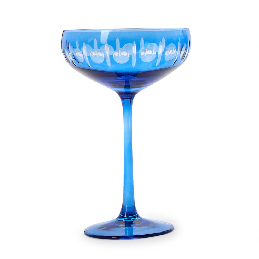 Cobalt blue hand-cut glass coupe cocktail glass centered on a white background featuring a vibrant translucent bowl with circular lens-cut patterns and a long slender stem