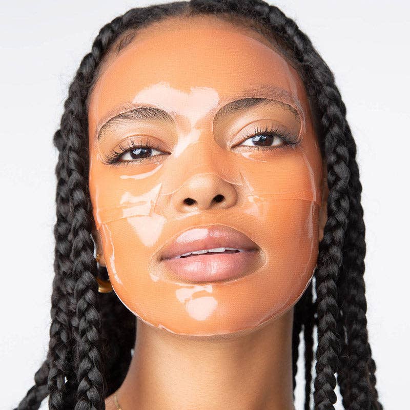 Commercial photograph of a Black woman with long dark braids wearing a glossy peach-toned translucent hydrogel face mask in a studio setting, highlighting the reflective texture and natural lashes