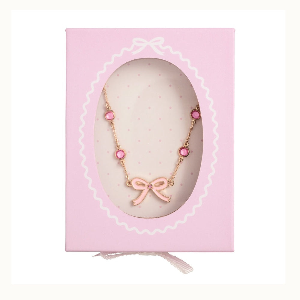 Gold-toned jewelry necklace featuring a pink enamel bow pendant and four circular pink gemstones displayed inside a decorative pink gift box with a scalloped oval window and subtle polka dot interior background