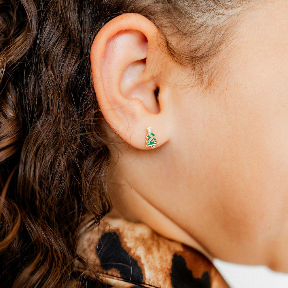 Photograph of a vibrant green enamel Christmas tree earring worn on a person's earlobe featuring a tiny gold star topper and shimmering gold garland details