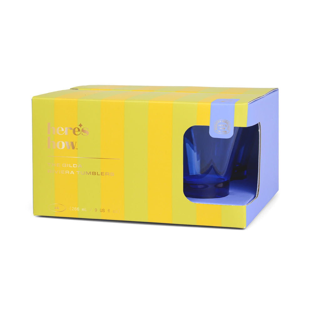 Product packaging by Here's How Modern Mixology for The Gilda Riviera Tumblers featuring vibrant yellow and lime green vertical stripes, gold foil lettering, and a cutout window showcasing a cobalt blue glass tumbler