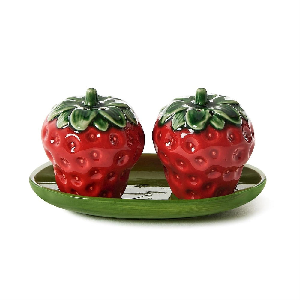 Ceramic strawberry salt and pepper shakers resting on a leaf-green tray featuring glossy red glazes, textured seed dimples, and sculpted green leaves against a neutral white background