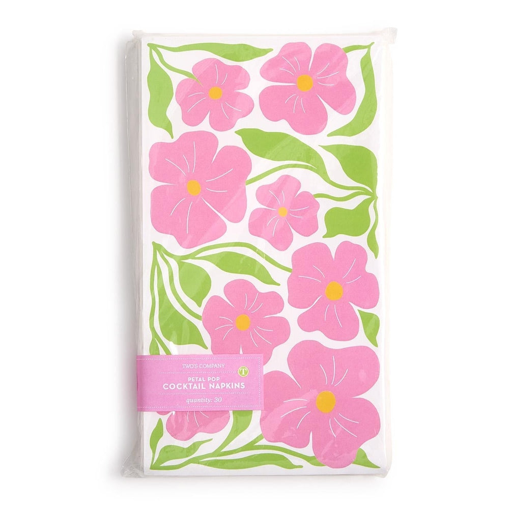 Paper cocktail napkins by Two's Company featuring a bold Petal Pop floral pattern with large pink blossoms, yellow centers, and bright green stems on a white background, packaged in a clear wrap with a pink paper band