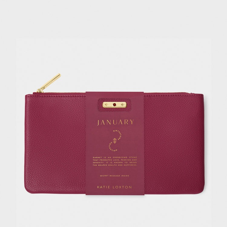 Product photograph by Katie Loxton of a garnet red vegan leather January birthstone pouch featuring a gold-toned zipper, pebbled texture, and a central paper sleeve with elegant gold foil lettering