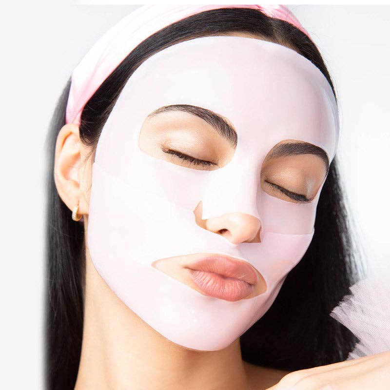Commercial photograph of a woman wearing a translucent light pink sheet mask in a studio setting featuring a matching pink headband and a small gold hoop earring