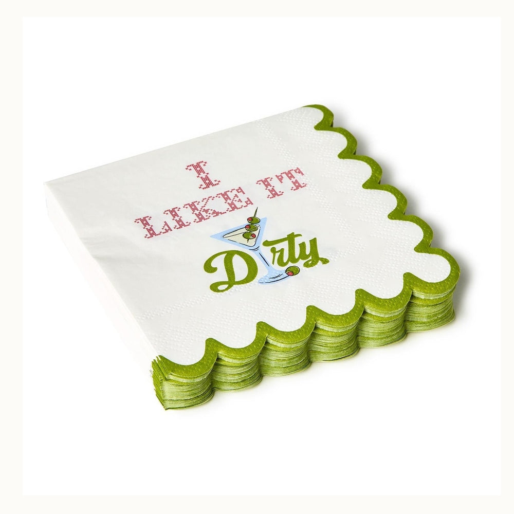 Printed paper cocktail napkins by August Morgan featuring a stack of white napkins on a plain background with scalloped green borders, red cross-stitch text reading I LIKE IT, and a martini glass illustration with three pimento olives next to a green script word Dirty