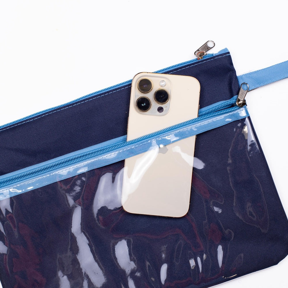 Product photograph of a navy blue canvas and clear vinyl pouch on a white background featuring a gold iPhone in the transparent pocket with light blue zipper tracks and metallic sliders