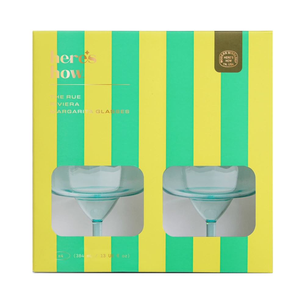 Product photography by Modern Mixology for a Rue Riviera Margarita Glass set featuring vibrant yellow and green vertical stripes, a gold foil brand seal, and die-cut windows showcasing two teal-tinted glass stems