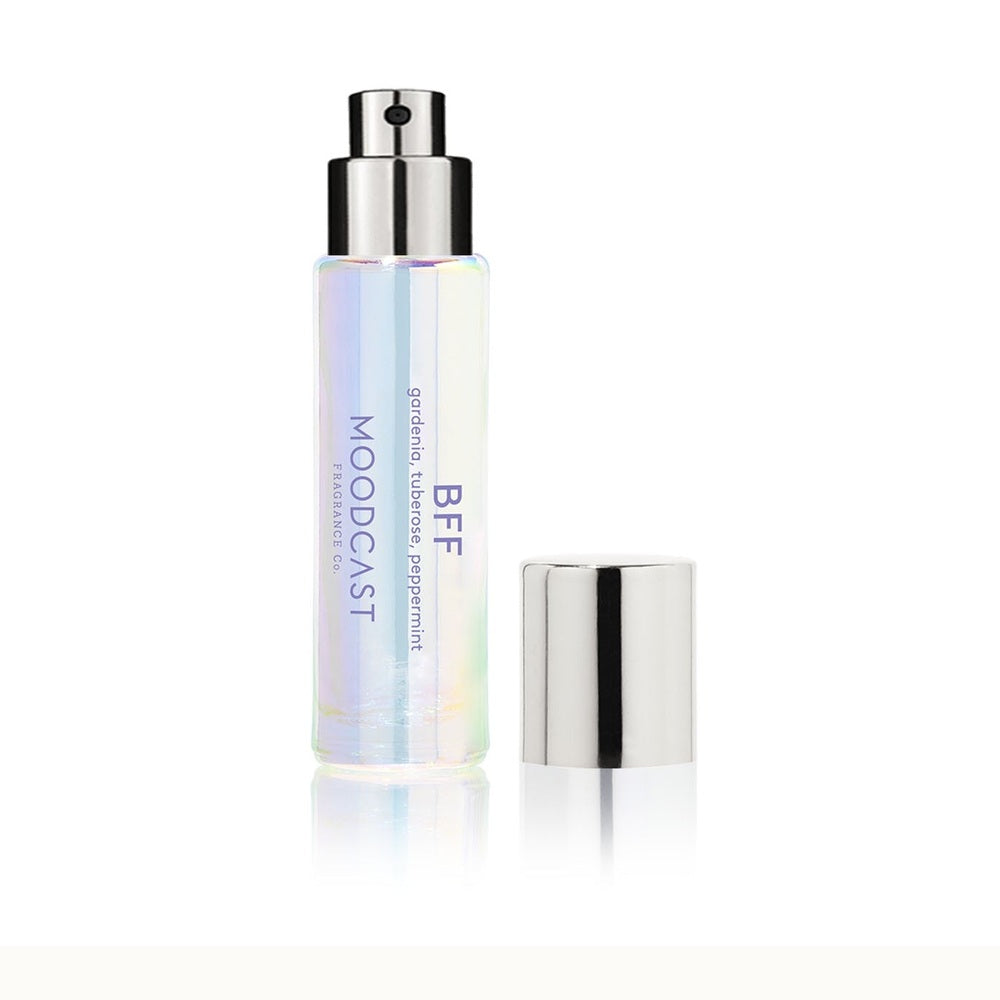 Product photograph by MOODCAST Fragrance Co of a BFF travel perfume spray on a white background featuring an iridescent glass bottle, a silver atomizer, and printed scent notes of gardenia, tuberose, and peppermint