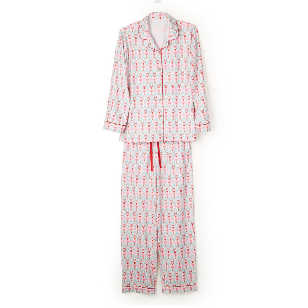 Studio product photograph of a two-piece pajama set against a white background featuring a festive nutcracker and light blue wreath pattern with red piping details and a matching red drawstring waistband
