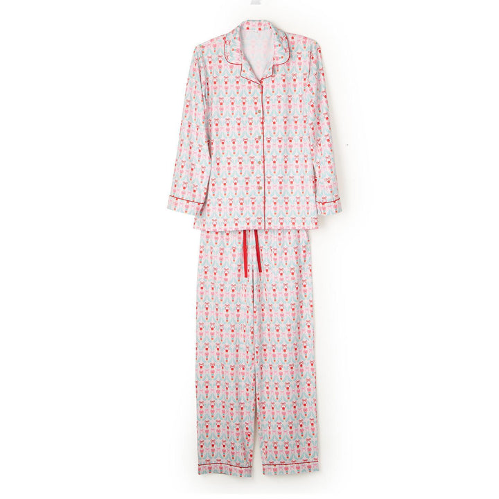 Studio product photograph of a two-piece pajama set against a white background featuring a festive nutcracker and light blue wreath pattern with red piping details and a matching red drawstring waistband