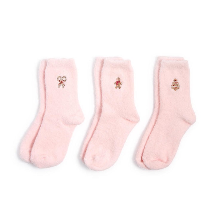 Studio product photograph of three pairs of light pink fuzzy socks on a white background featuring embroidered holiday motifs of a candy cane with a red bow, a gingerbread man, and a decorated Christmas tree