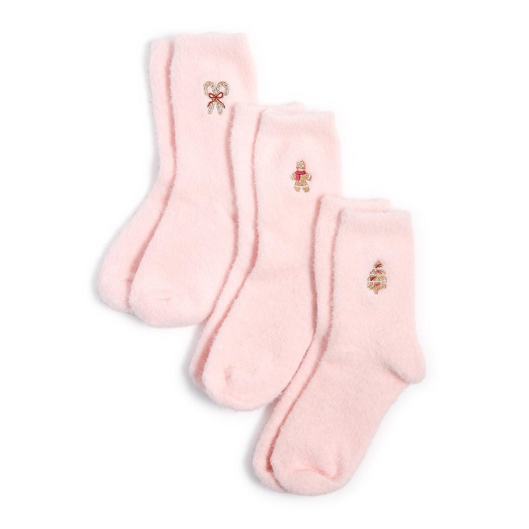 Studio photography of three pairs of light pink fuzzy socks on a white background featuring holiday embroidery of candy canes with a red bow, a gingerbread man with a scarf, and a decorated Christmas tree