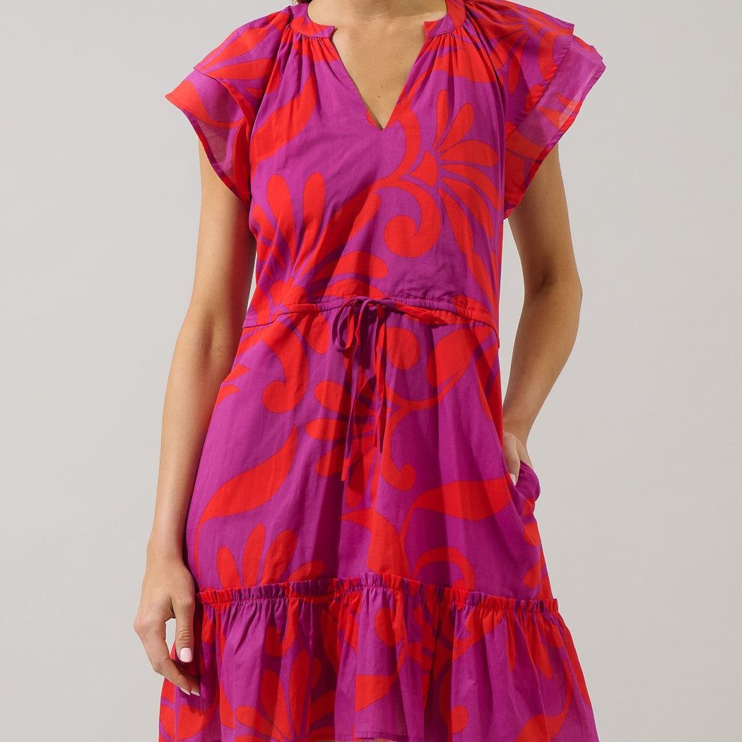 Studio fashion photograph of a woman wearing a vibrant magenta midi dress with a bold red floral pattern featuring flutter sleeves, a drawstring waist, and a ruffled tiered hem in a studio setting