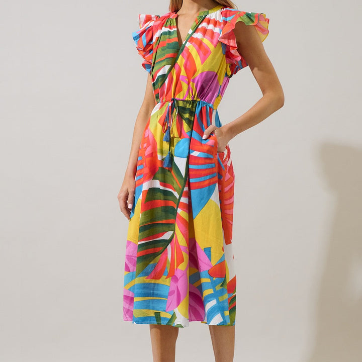 Studio fashion photograph of a woman wearing a vibrant tropical print midi dress featuring ruffled butterfly sleeves and a drawstring waist with blue tassels in a neutral studio environment