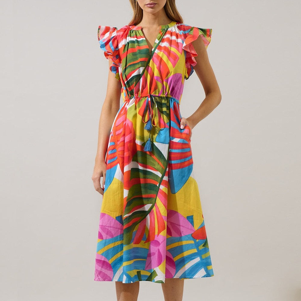Studio photograph of a woman posing against a neutral backdrop wearing a vibrant tropical leaf print midi dress featuring fluttery ruffle sleeves and a blue tasseled drawstring waist