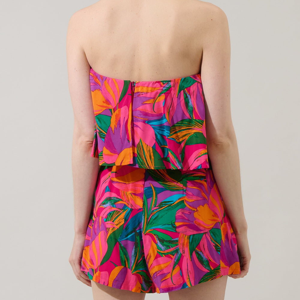 Studio photograph of a model viewed from behind against a plain backdrop wearing a vibrant tropical floral two-piece set featuring a strapless peplum top with a back zipper and matching colorful shorts