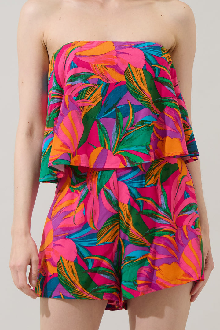 Photograph of a model in a studio wearing a vibrant tropical print two-piece set featuring a strapless ruffled top and matching shorts with neon pink, orange, and teal palm leaf patterns