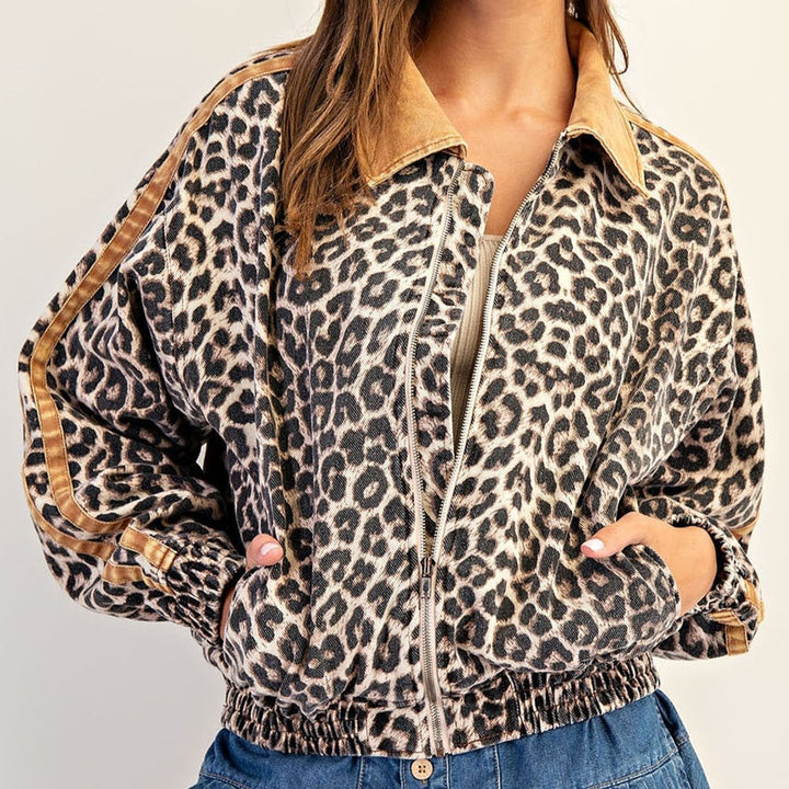 Photograph of a woman wearing a leopard print bomber jacket in a studio featuring a tan corduroy collar, brown side-stripe sleeve details, and a metallic silver zipper