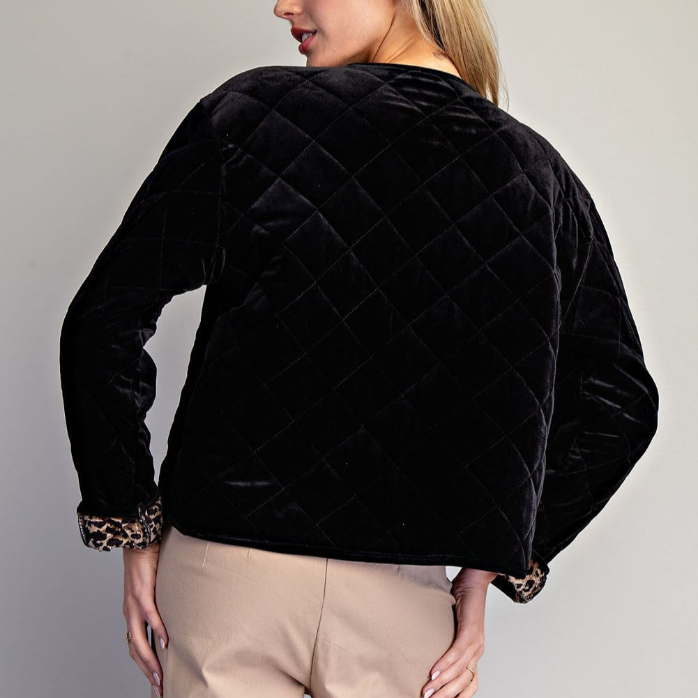 Fashion photography of a woman in a studio showcasing a black diamond-quilted velvet jacket featuring leopard print lining at the cuffs and beige tailored trousers