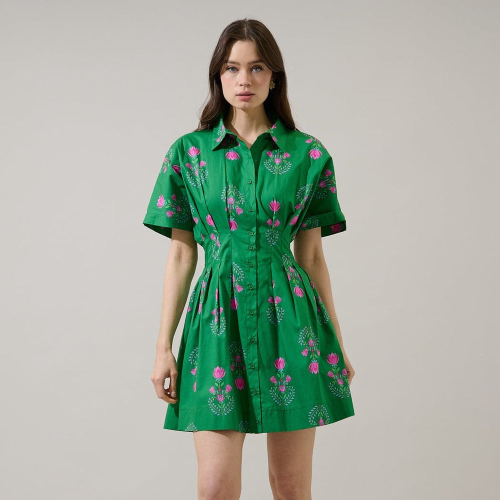 Digital studio photograph of a woman wearing a vibrant emerald green mini dress with a pink lotus floral pattern, button-down front, and cinched pleated waist against a neutral backdrop