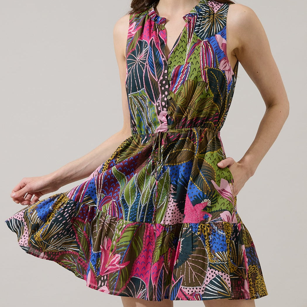 Photograph of a Farm Rio dress on a woman in a studio setting showcasing a vibrant botanical print with pink flowers, a tiered skirt, and a ruffled V-neckline