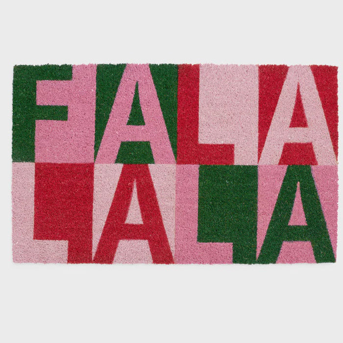Coir fiber doormat featuring the repeating phrase FA LA LA LA in a modern color-blocked layout of forest green, light pink, and festive red presented on a neutral studio background