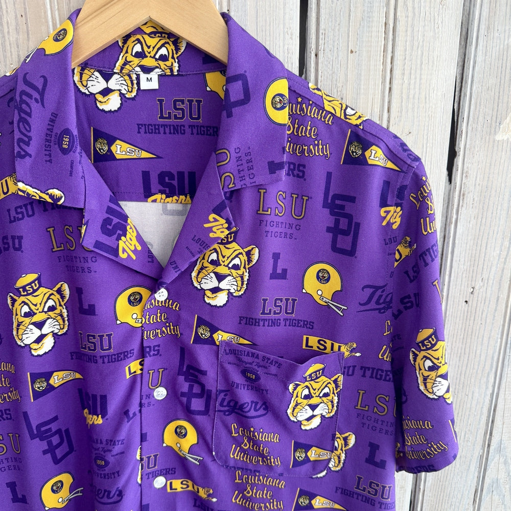 LSU branded purple button-down shirt featuring the iconic Mike the Tiger mascot and yellow football helmets hanging on a wooden hanger against a weathered white wooden background with white buttons and a patterned breast pocket