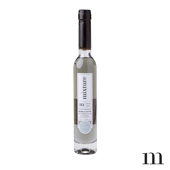 Studio photograph of Mixture brand bubble bath in a tall slender glass bottle with a black screw cap and minimalist No. 27 Cashmere label on a white background