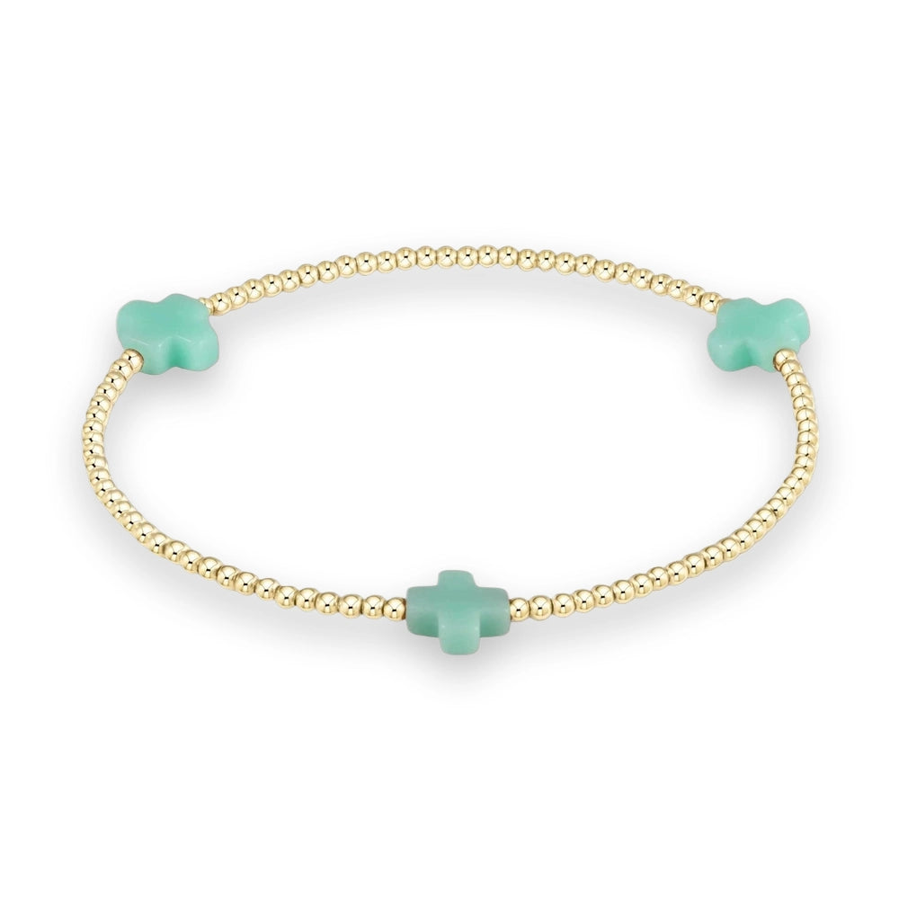 Gold and gemstone beaded bracelet featuring three matte mint green cross charms spaced evenly among polished metallic spheres against a neutral cream studio background
