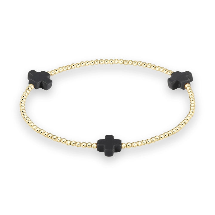 Gold beaded bracelet by Erimish featuring three matte black cross charms interspersed between polished gold-toned spherical beads on a neutral cream background
