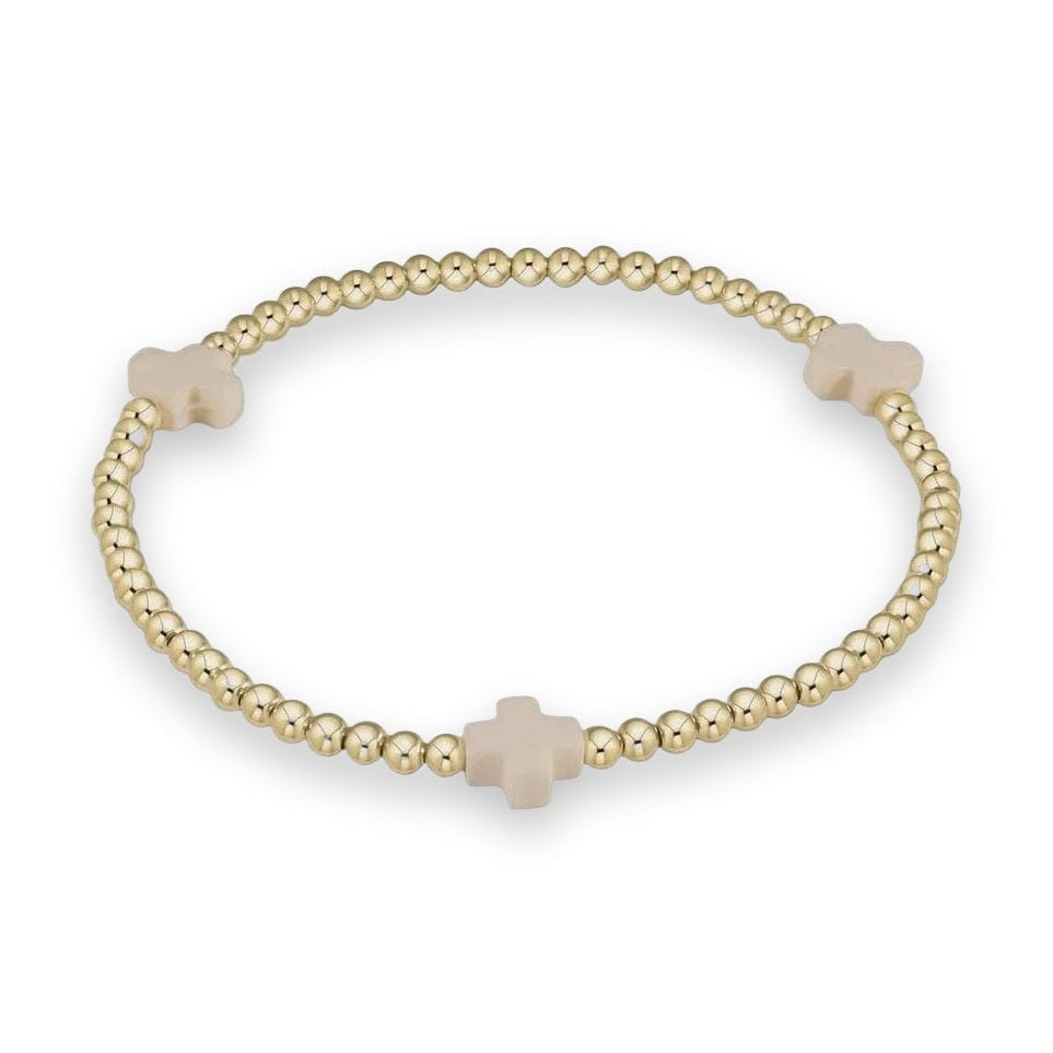 A gold beaded stretch bracelet with three cream-colored cross charms, displayed on a clean white background.