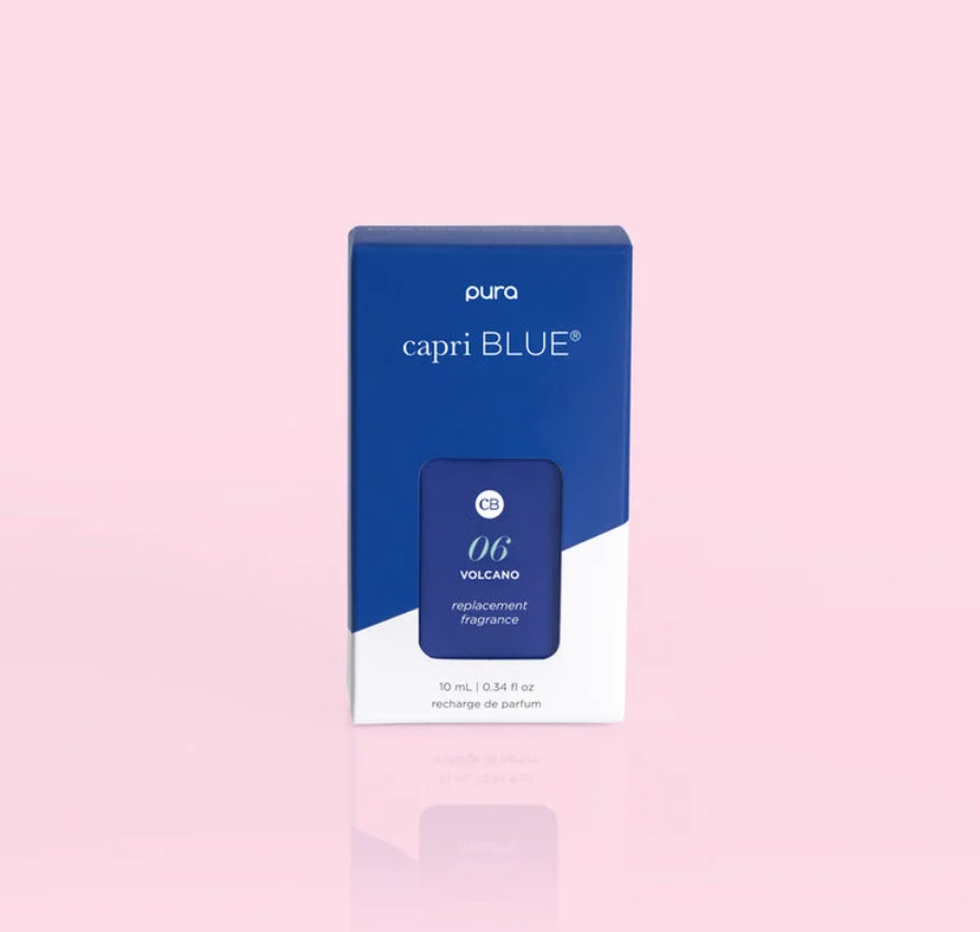 Digital product photograph of a Pura Capri Blue Volcano replacement fragrance box on a pastel pink background featuring cobalt blue packaging with white branding and a subtle mirrored reflection
